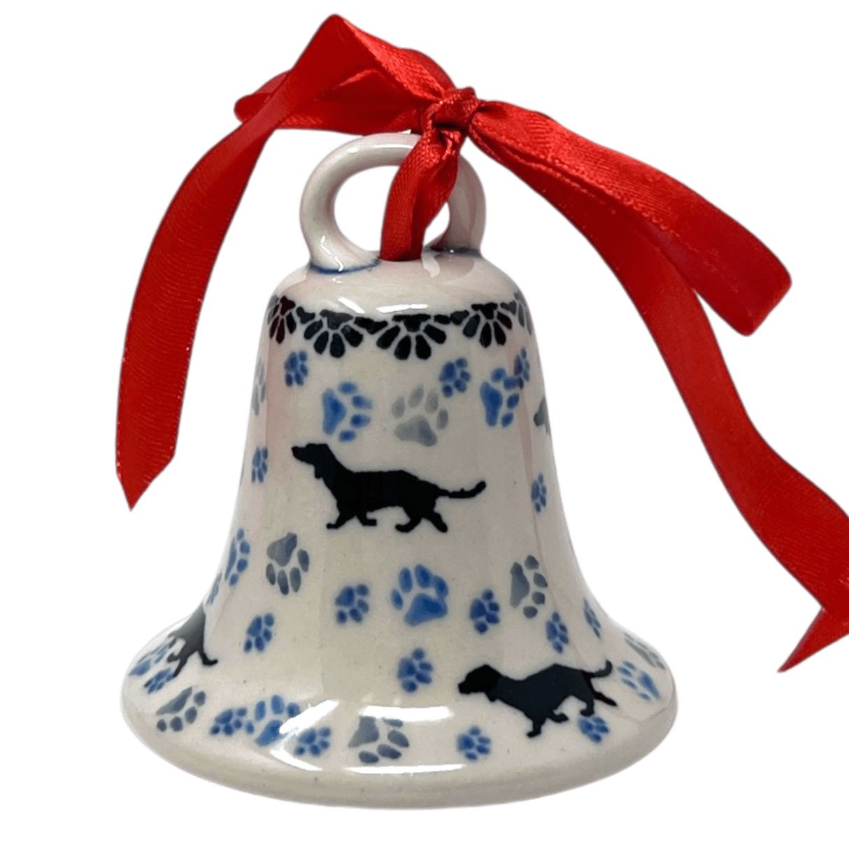 A Polish pottery small ceramic bell ornament with a white base decorated with blue paw prints, black dog silhouettes, and a red ribbon loop at the top, shown on a plain white background.