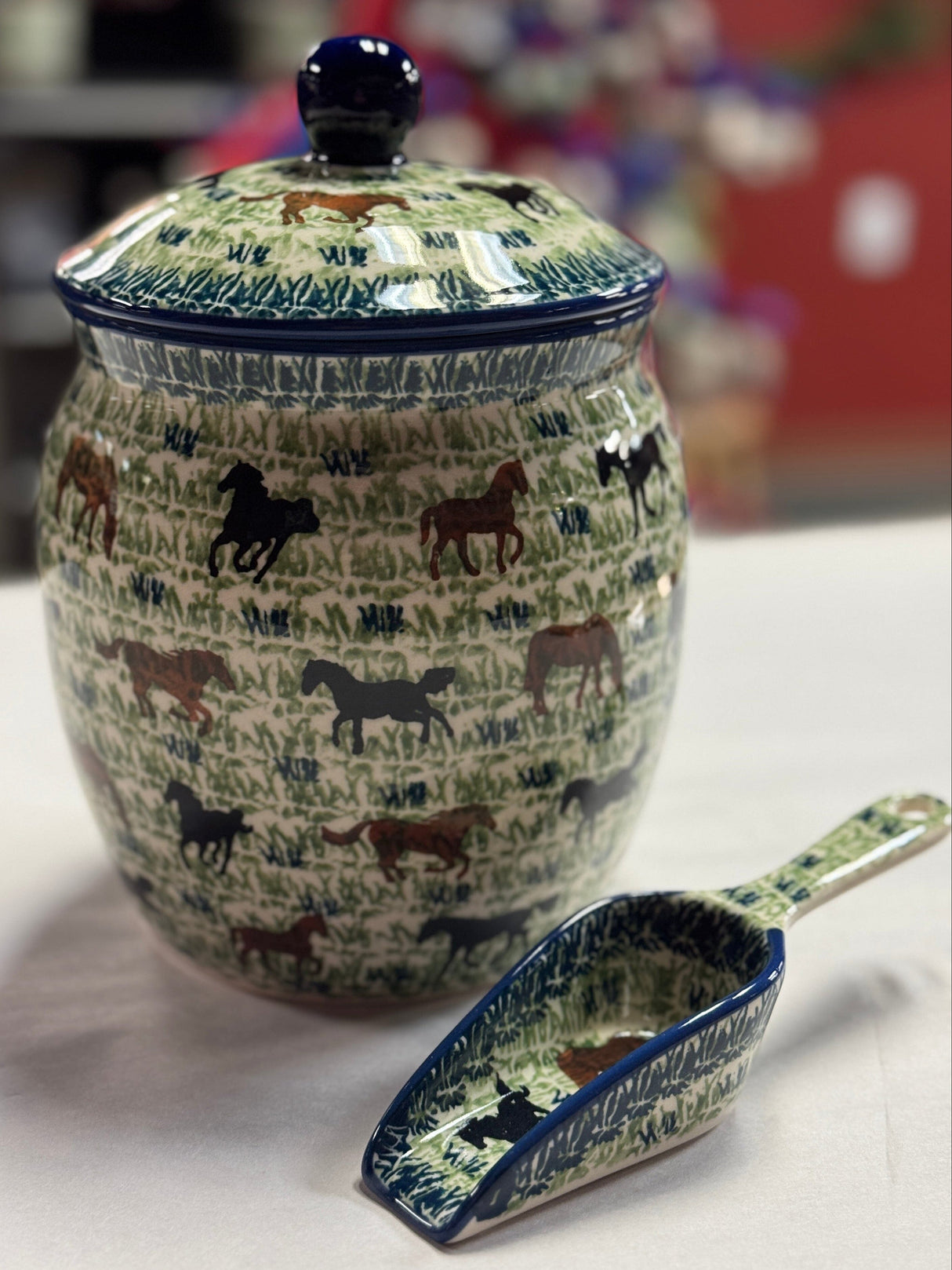 Ceramic jar with horse design and matching scoop on a white surface